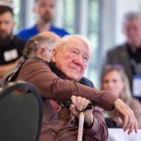 President Emeritus Don Lubbers listens to rowing speech while rest arm on cane